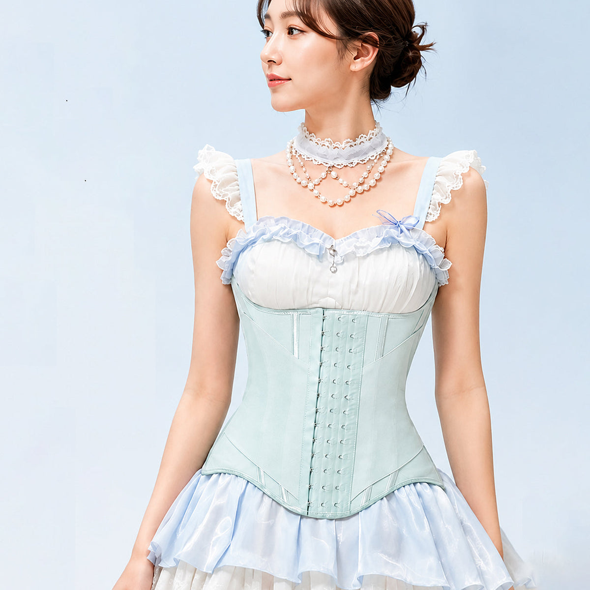 A woman wearing a light blue and white corset-style dress top with ruffled lace straps, layered pearl necklaces, and a pale blue ruffled skirt against a soft light blue background.