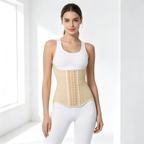 A woman modeling a beige waist trainer corset over a white tank top and white leggings in a bright, minimalist white room.