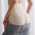 Rear view of a person wearing a high-waisted beige shapewear brief and gray denim jeans against a soft white curtain background.