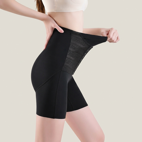 A model wearing black high-waisted compression shorts, lifting the waistband to show the elastic and mesh support panel, against a solid light beige background.