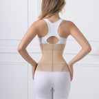 A woman shown from the back wearing a beige waist trainer corset over a white sports bra and white leggings, set against a white paneled wall.
