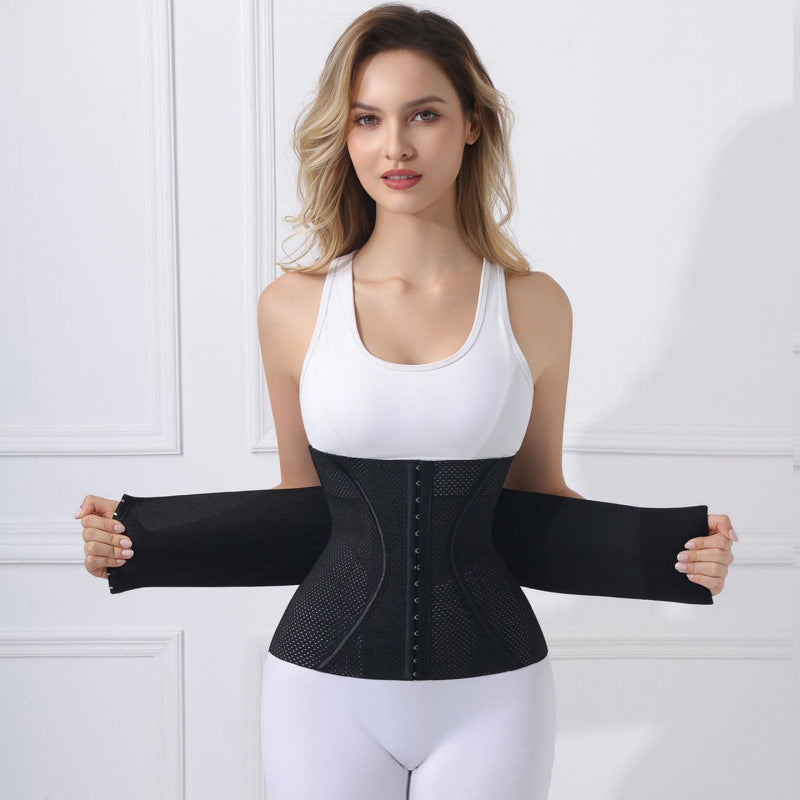 A woman modeling a black waist trainer belt with built-in sleeves, shown against a white paneled wall background.