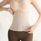 A woman wearing a beige waist trainer shapewear belt over a nude bra and dark brown leggings, shown from the chest down against a clean white background.