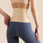 Rear view of a model wearing a beige waist trainer belt over blue leggings, set against a solid beige background.