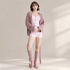 A woman models a coordinated lounge set consisting of a light pink bodysuit, a dusty mauve zip-up hoodie, matching mauve knee-high socks, and nude flat sandals against a warm beige studio backdrop with soft window shadows.