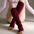 A model wearing burgundy cable-knit leg warmers with open toes, paired with a light pink long-sleeve top, posed against a neutral beige studio background.