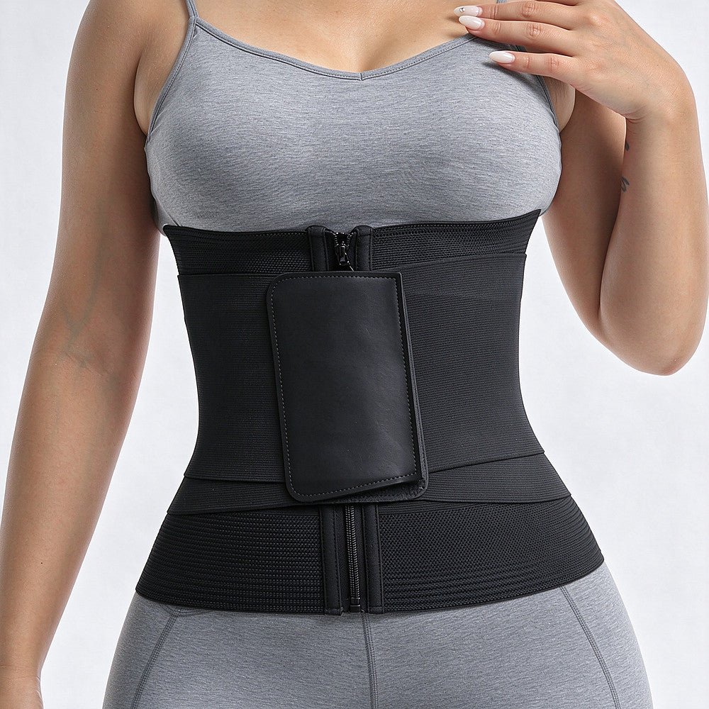A black waist trainer belt with a front zipper and a large rectangular patch pocket, shown worn by a model in a gray sports bra and leggings against a light gray studio background.