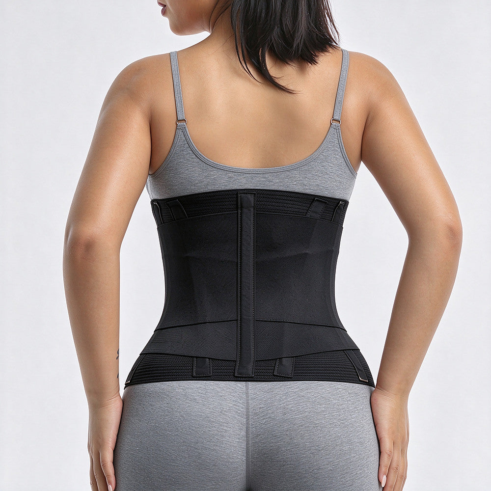 A woman shown from the back wearing a black waist trainer or waist support belt over a gray sports bra and gray leggings against a light gray studio background.