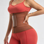 A woman wearing a brown waist trainer belt with a zippered front and a side pocket, paired with a coral sports bra and matching leggings, against a light gray studio background.