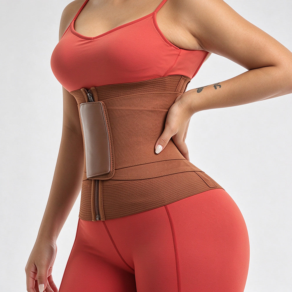 A woman wearing a brown waist trainer belt with a zippered front and a side pocket, paired with a coral sports bra and matching leggings, against a light gray studio background.