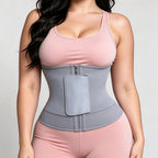 A woman wearing a light gray waist trainer belt with a front zipper and a large rectangular pocket, paired with a pink sports bra and matching pink leggings, against a light gray studio background.