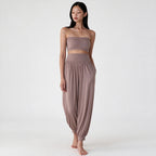 A woman modeling a matching two-piece lounge set in a dusty mauve color, featuring a strapless bandeau crop top and high-waisted harem pants, against a plain white studio background.