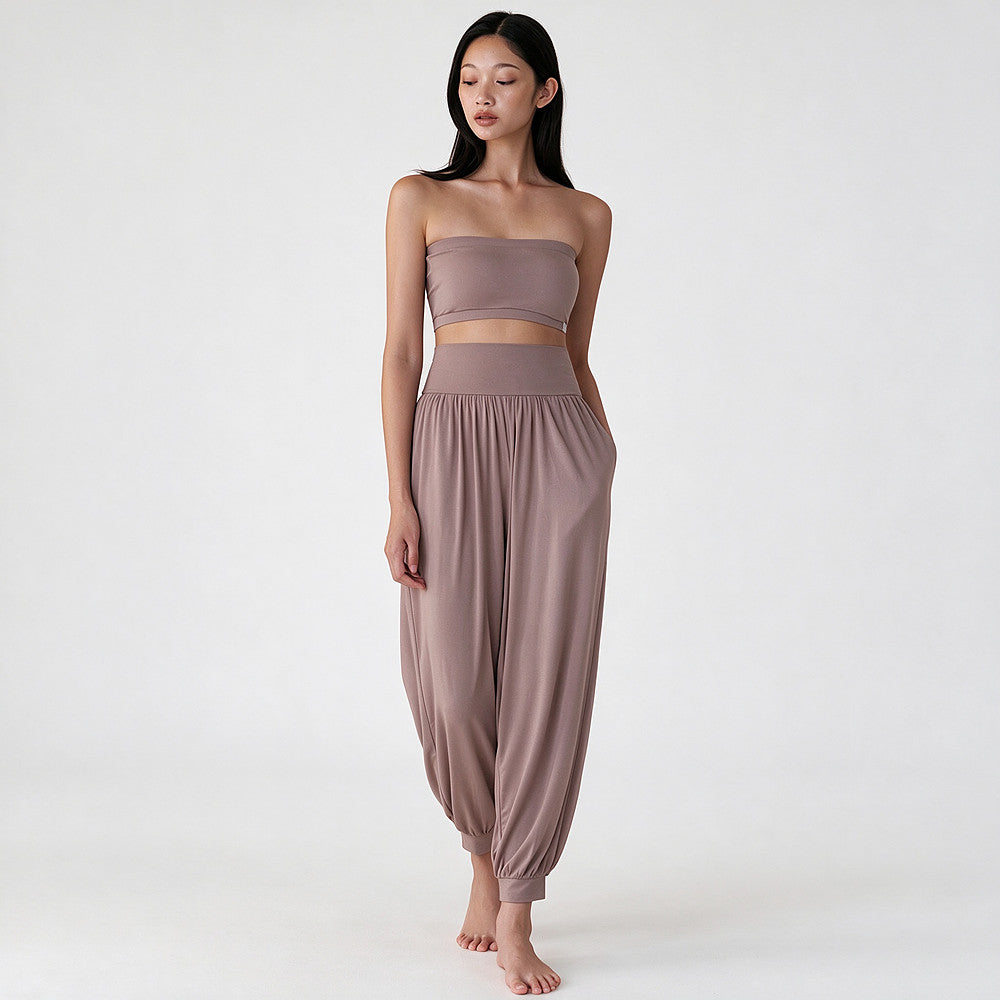 A woman modeling a matching two-piece lounge set in a dusty mauve color, featuring a strapless bandeau crop top and high-waisted harem pants, against a plain white studio background.
