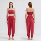 A model is shown from the front and back wearing a matching two-piece lounge set in a dusty rose red color. The set includes a strapless bandeau-style crop top and high-waisted, loose harem-style pants with elastic cuffs.