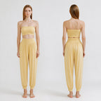 A model is shown from the front and back wearing a pale yellow two-piece lounge set consisting of a strapless bandeau-style crop top and matching high-waisted harem pants, against a plain light gray studio background.