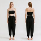 A model is shown from the front and back wearing a black two-piece outfit consisting of a strapless bandeau-style crop top and high-waisted loose harem pants, against a plain light background.