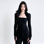 A woman modeling a black long-sleeve knit top with a square neckline and matching black pants against a plain light gray studio background.