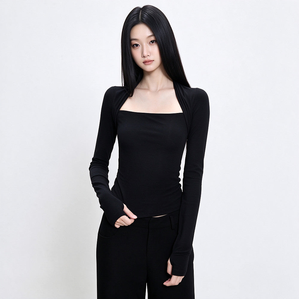 A woman modeling a fitted black long-sleeve top with a square neckline and long sleeves, paired with black pants, against a plain light gray studio background.