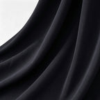 A close-up of draped black fabric with soft folds and a subtle sheen, shown against a light neutral background.