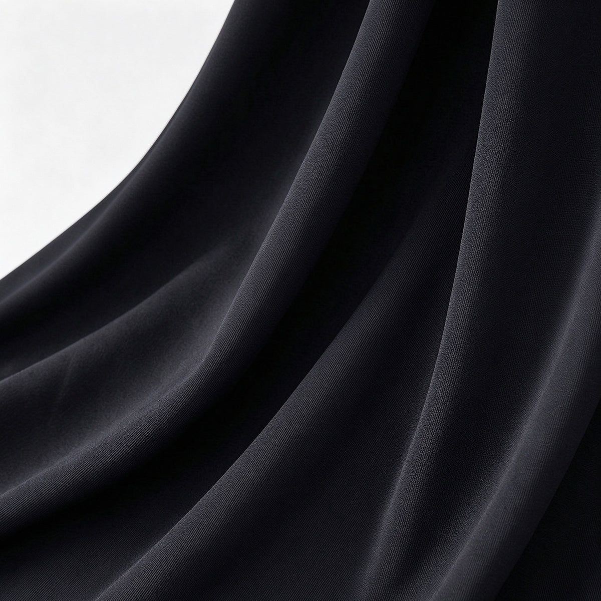 A close-up of draped black fabric with soft folds and a subtle sheen, shown against a light neutral background.