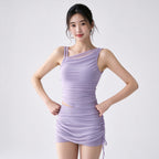 A woman modeling a lavender ruched one-shoulder mini dress with a sheer mesh panel on the upper chest, photographed against a plain light gray studio background.